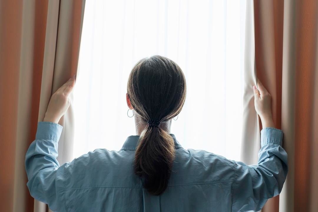 kobieta posiada okna plastikowe opole w domu. Wygląda przez nie i trzyma zasłony